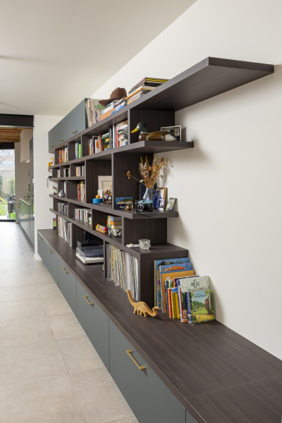 Maatwerk boekenkast in donkere houttint met open vakken en decoratie. Functionele opbergoplossing voor een modern interieur.